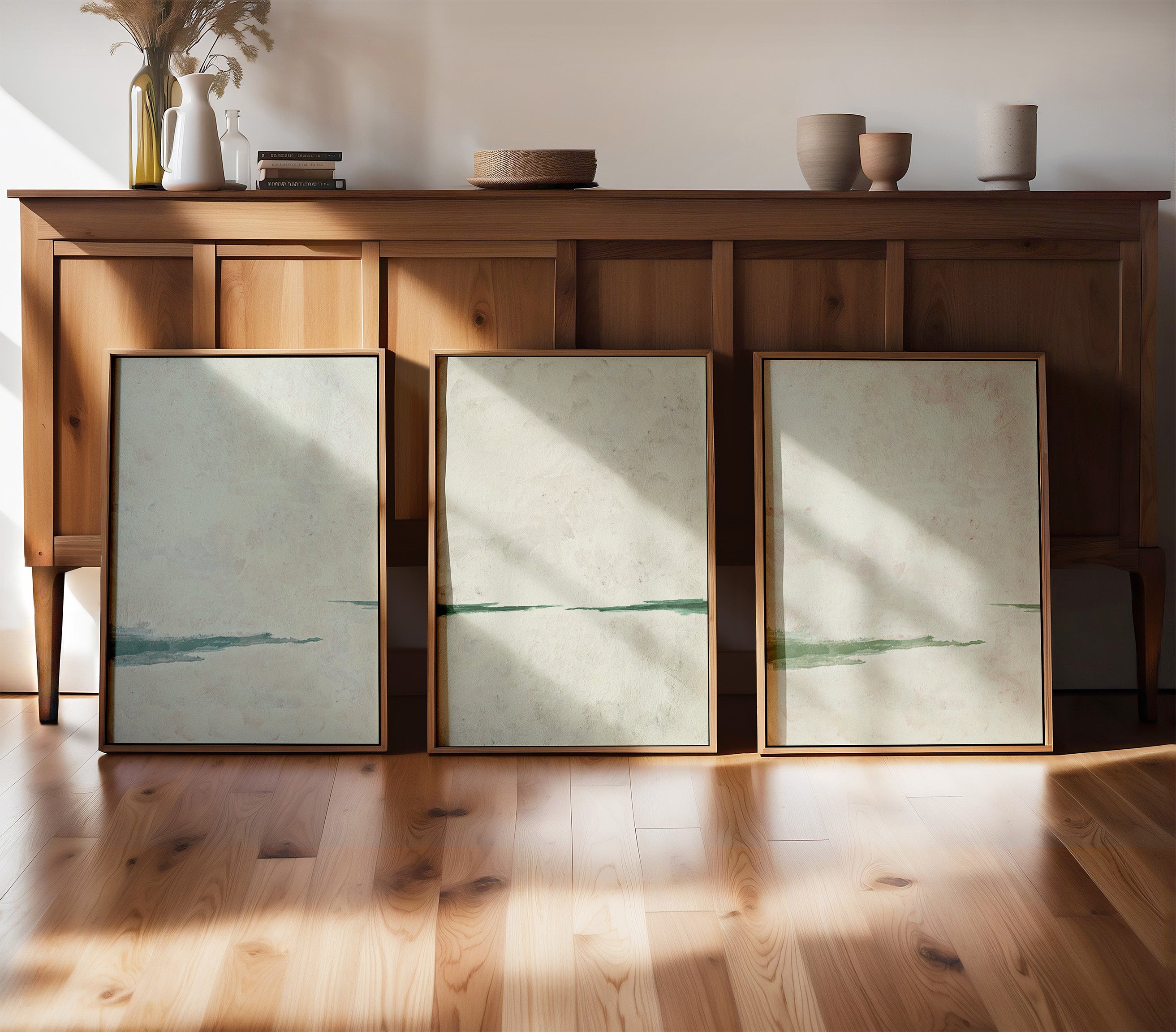 House of Gallerista - Triptychon aus minimalistischen Wandbildern in sanften Grüntönen: Zeitlose Eleganz in natürlichen Holzrahmen, präsentiert vor einem rustikalen Sideboard und warmem Holzboden. Perfekt für eine harmonische Raumgestaltung. Entdecke den House of Gallerista Wandbild-Konfigurator für individuelle Kunstwerke. Schlüsselwörter: House of Gallerista, Wandbild, minimalistisches Design, Holzrahmen, Wandbild-Konfigurator, Interior Design, Triptychon, Grüntöne.